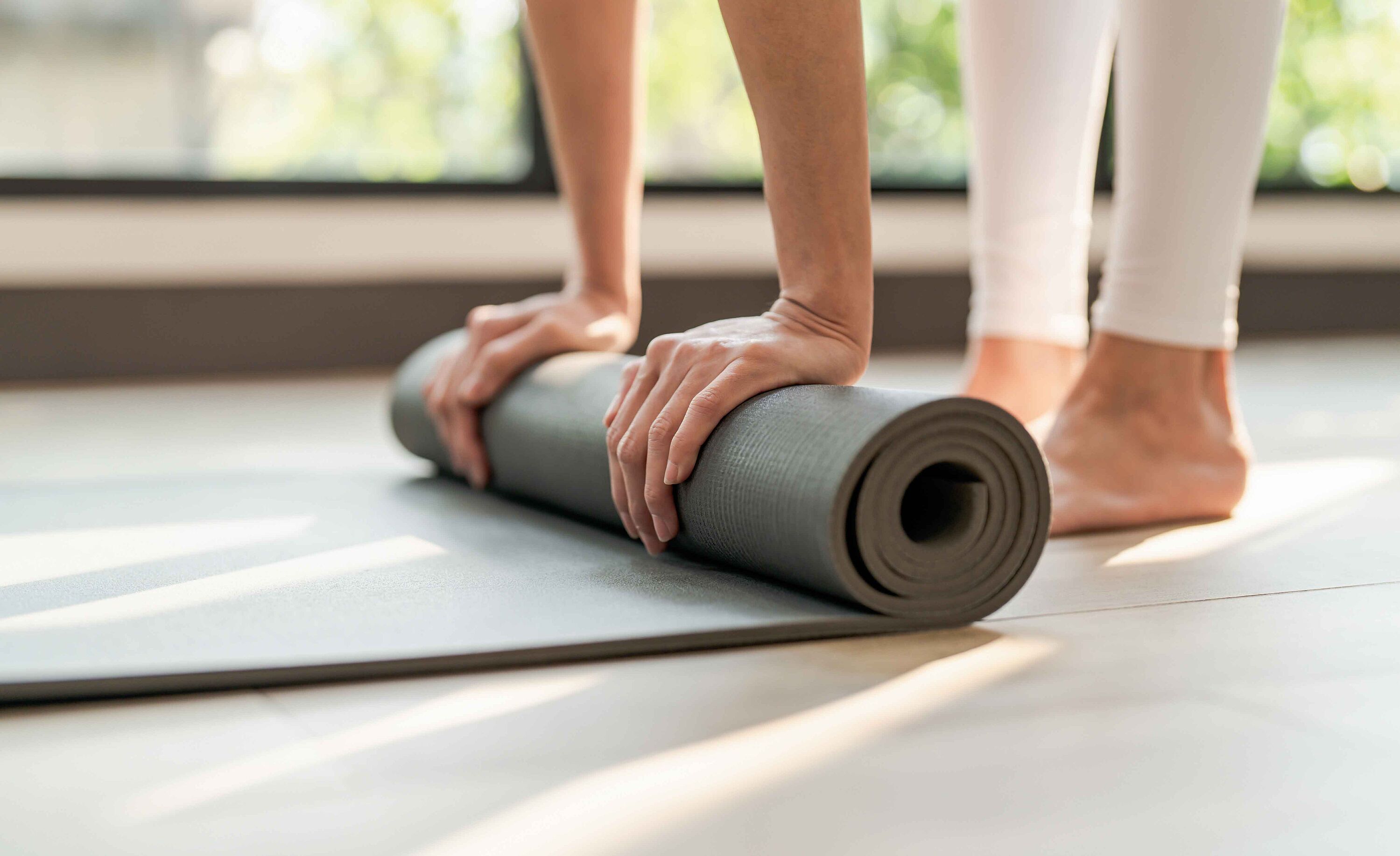 Bild zeigt Detailansicht, wie eine Frau eine Yogamatte ausrollt.